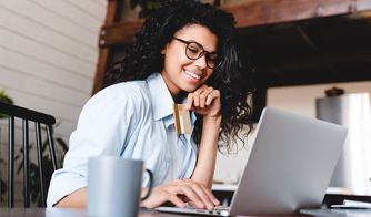 Compra online con tarjeta de crédito Mujer sonriendo mientras paga con tarjeta frente a su portátil